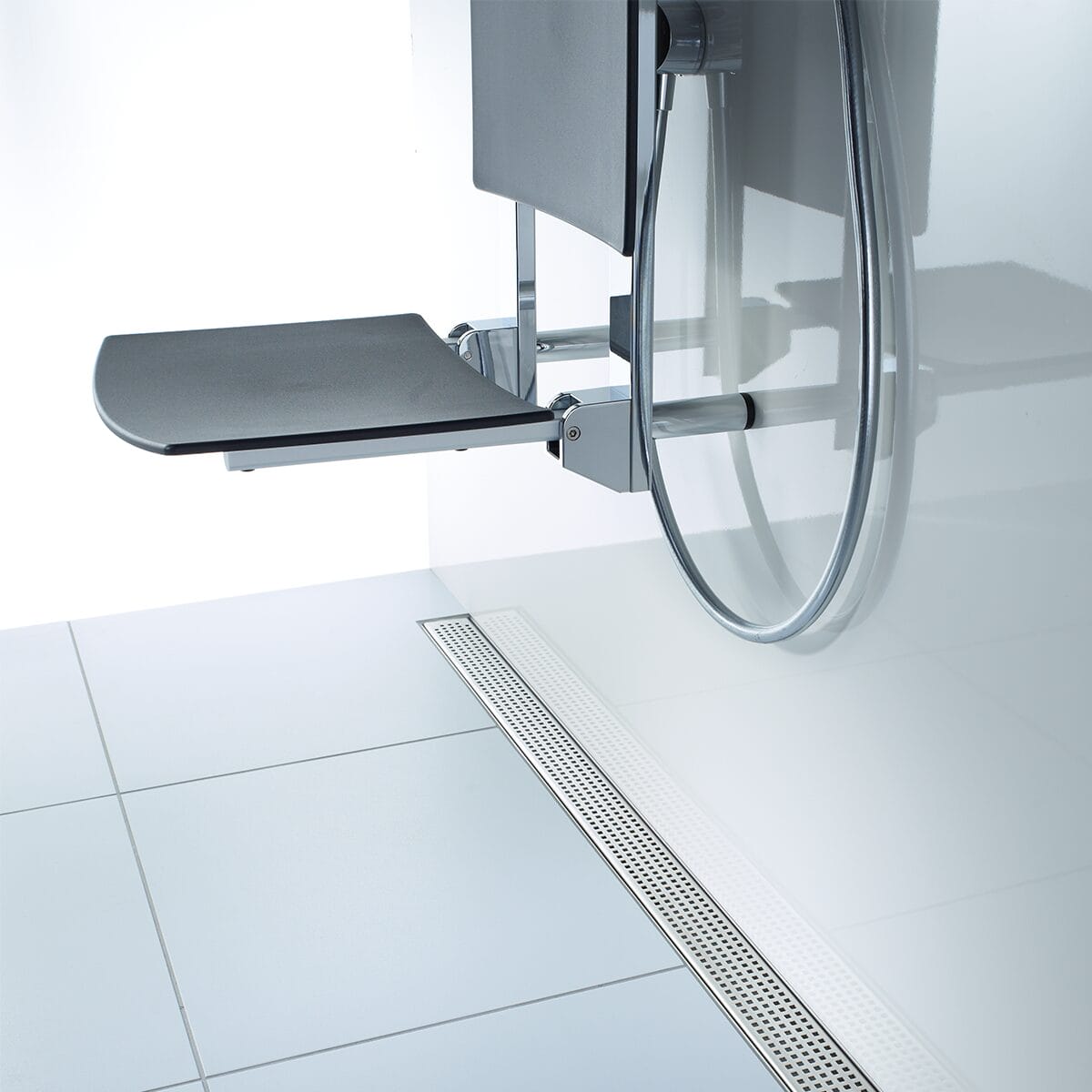Barrierefreie Dusche mit ACO ShowerDrain C Duschrinne mit silbernem Quadrato Designrost neben klappbarem Duschsitz