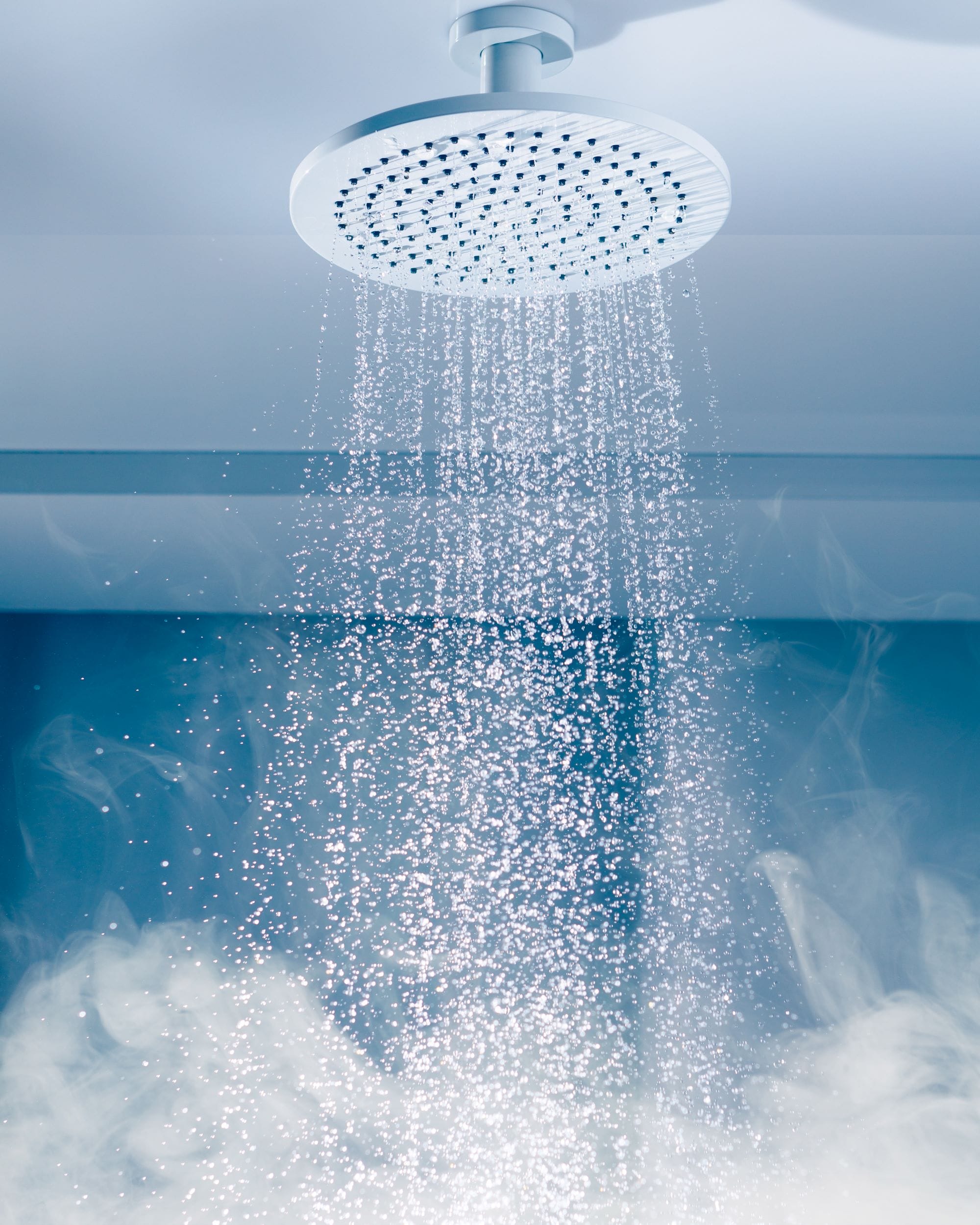 Wasserstrahl aus einer Decken-Regendusche mit feinem Sprühbild und aufsteigendem Dampf
